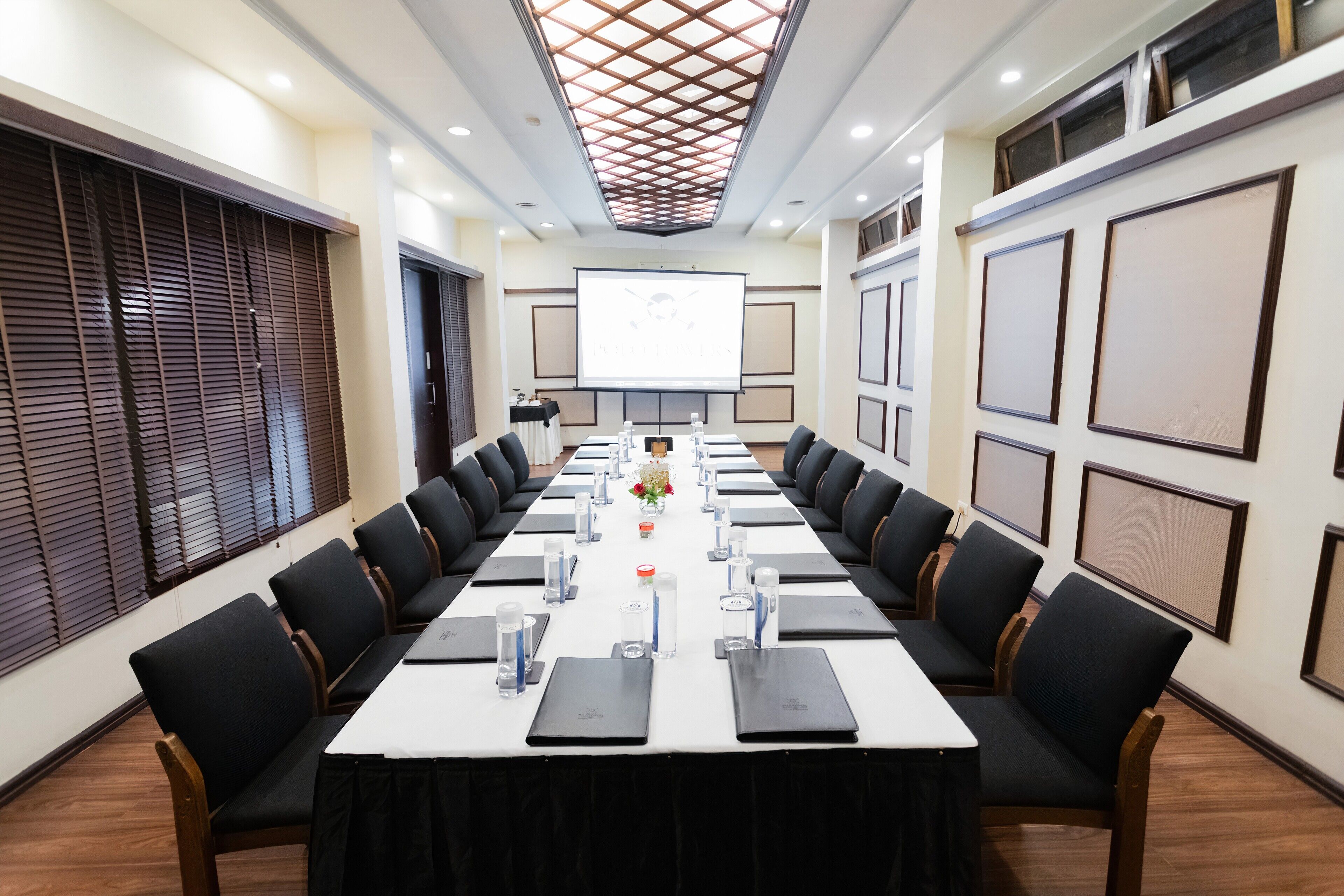 Un salón de conferencias con una larga mesa, sillas negras y una pantalla para proyector.