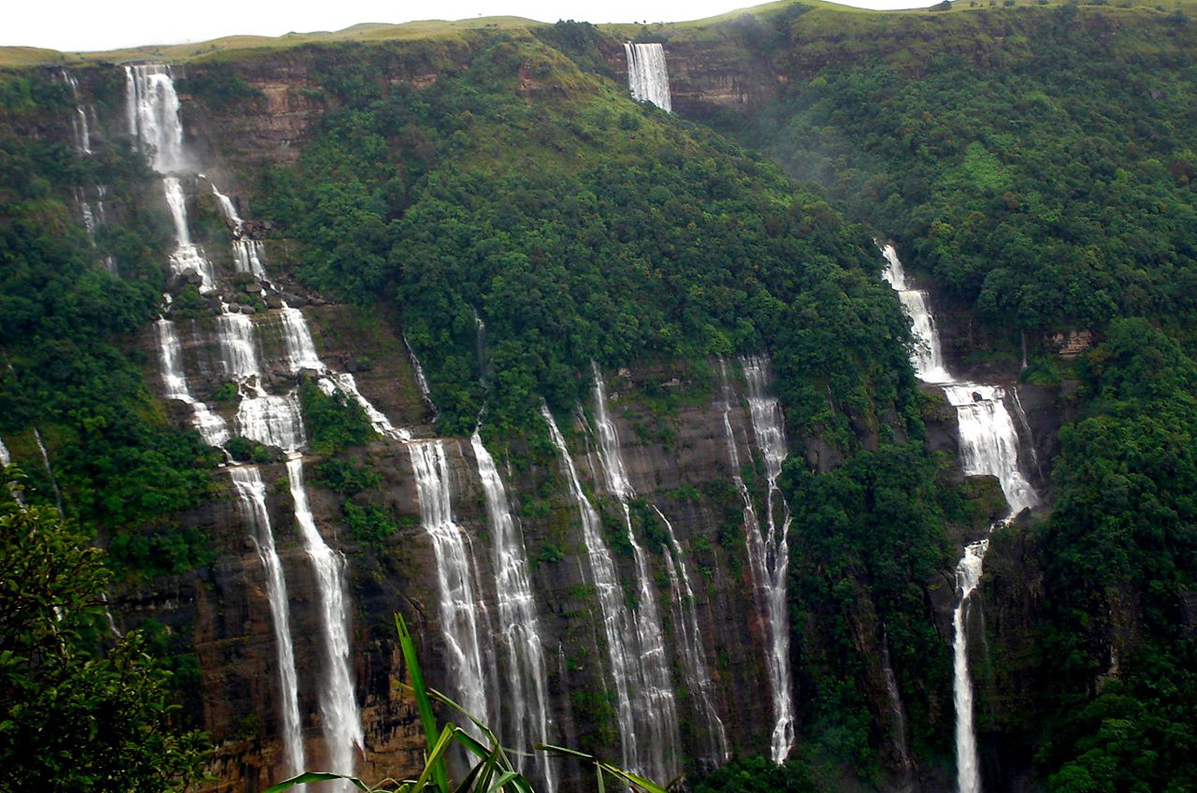 A large waterfall cascading down a steep cliff surrounded by dense green forest.