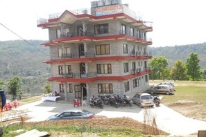 A multi-story building with balconies, a sign indicating it is a hotel, and parked vehicles in front. - Dhampus Resort (Pokhara)