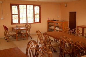 A dining area with a long wooden table and wicker chairs, a window with bars, and a wooden cabinet with shelves. - Dhampus Resort (Pokhara)