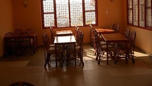 Un coin repas avec une grande table et des chaises, une fenêtre avec des barreaux et un luminaire fixé au mur.