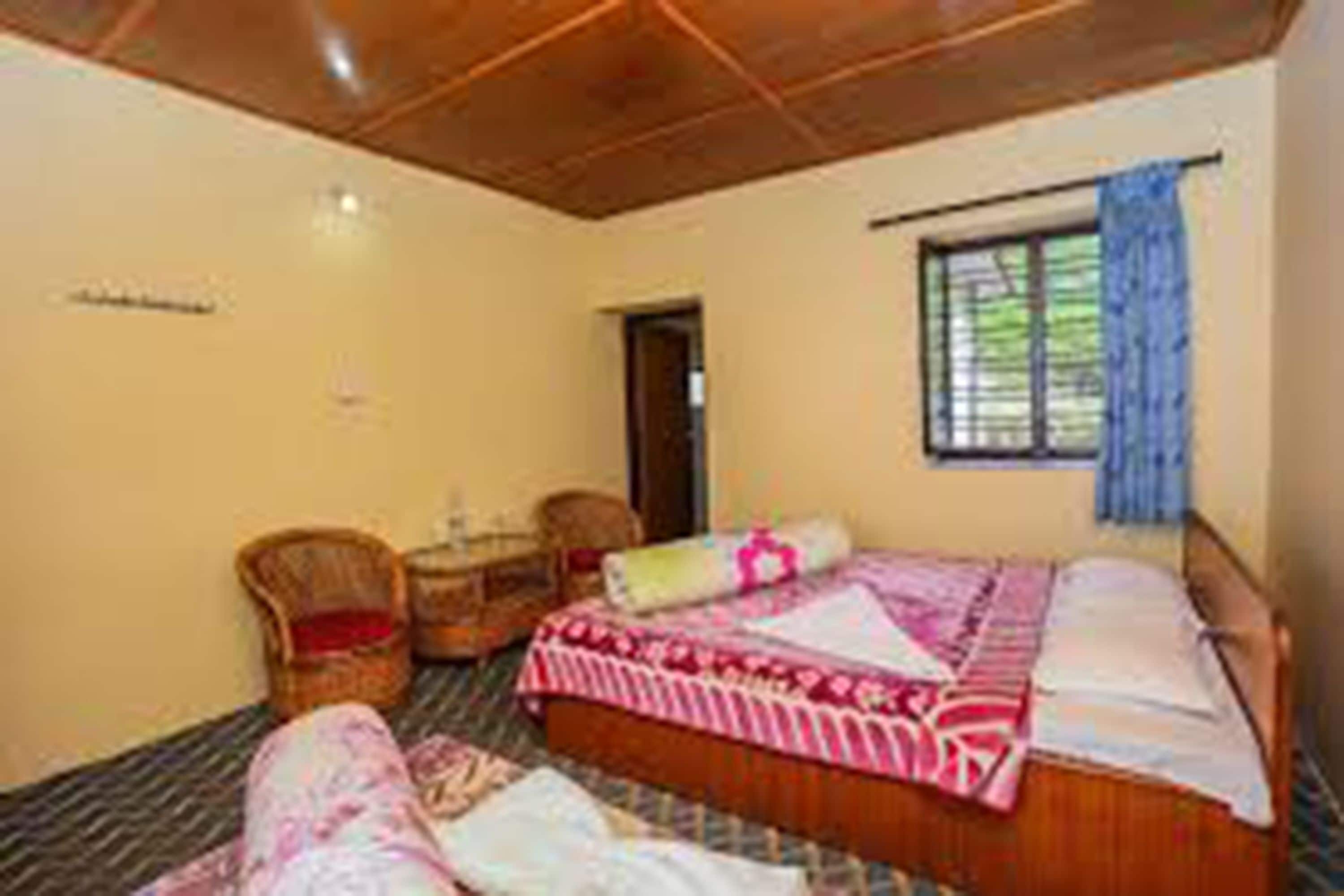 A room with a bed, a chair, a small table, and a window with curtains.
