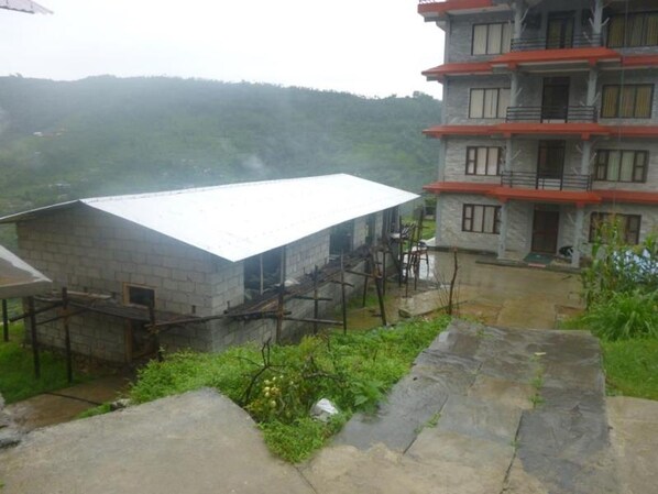 A multi-story building with a red roof, surrounded by greenery and a stone pathway. - Dhampus Resort (Pokhara)