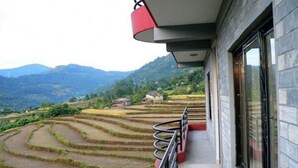Un bâtiment doté d’un balcon donnant sur des champs en terrasses et des montagnes.