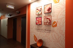 A hotel corridor with a sign indicating the direction to the Downey room, a wall with framed pictures of food, and a welcome message. - WATERGATE Ichinomiya (Inazawa)