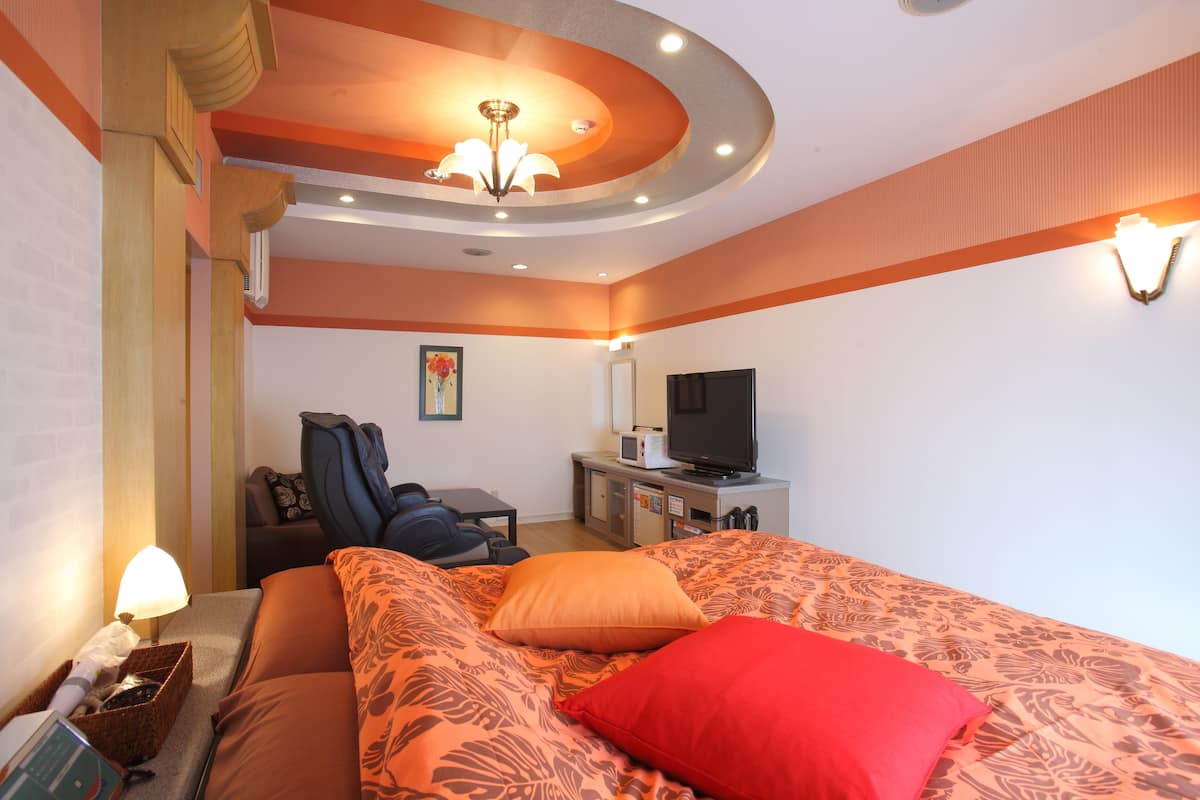 Quarto de hotel com cama, escrivaninha, televisão e cadeira de massagem.