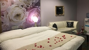Et hotelværelse med et stort blomstermotiv, en seng med rosenblade, en sofa og et lille bord med en flaske.