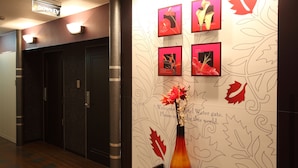 En hotellobby med en reception, en vase med blomster, og en væg med bladmotiver og et velkommenskilt.