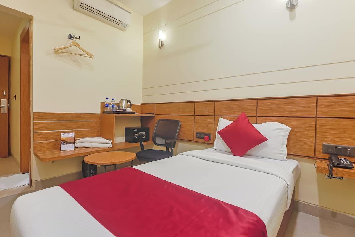 Habitación de hotel con cama, escritorio, silla, mesita, estante con artículos de tocador y teléfono en la pared.