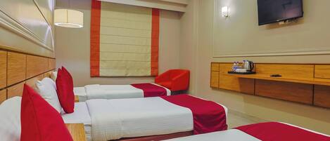 A hotel room with two beds, red and white bedding, a television on the wall, and a wooden cabinet with a kettle.