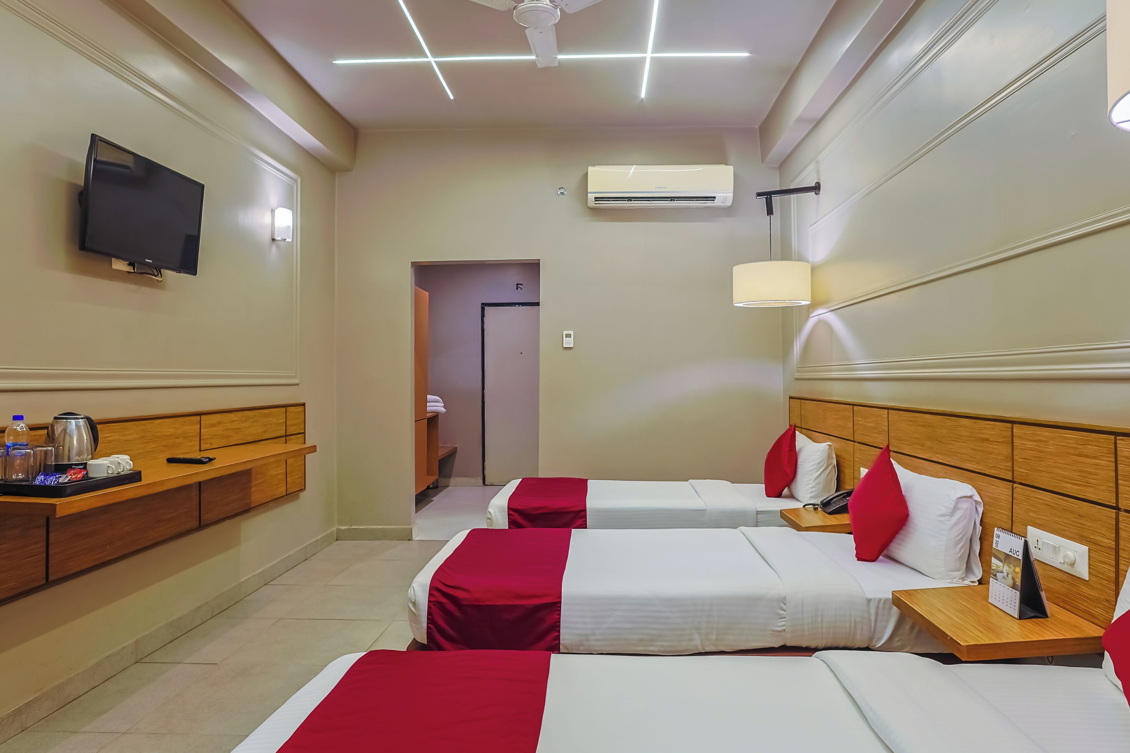 A hotel room with two beds, a TV, a desk with a lamp, and an air conditioning unit.
