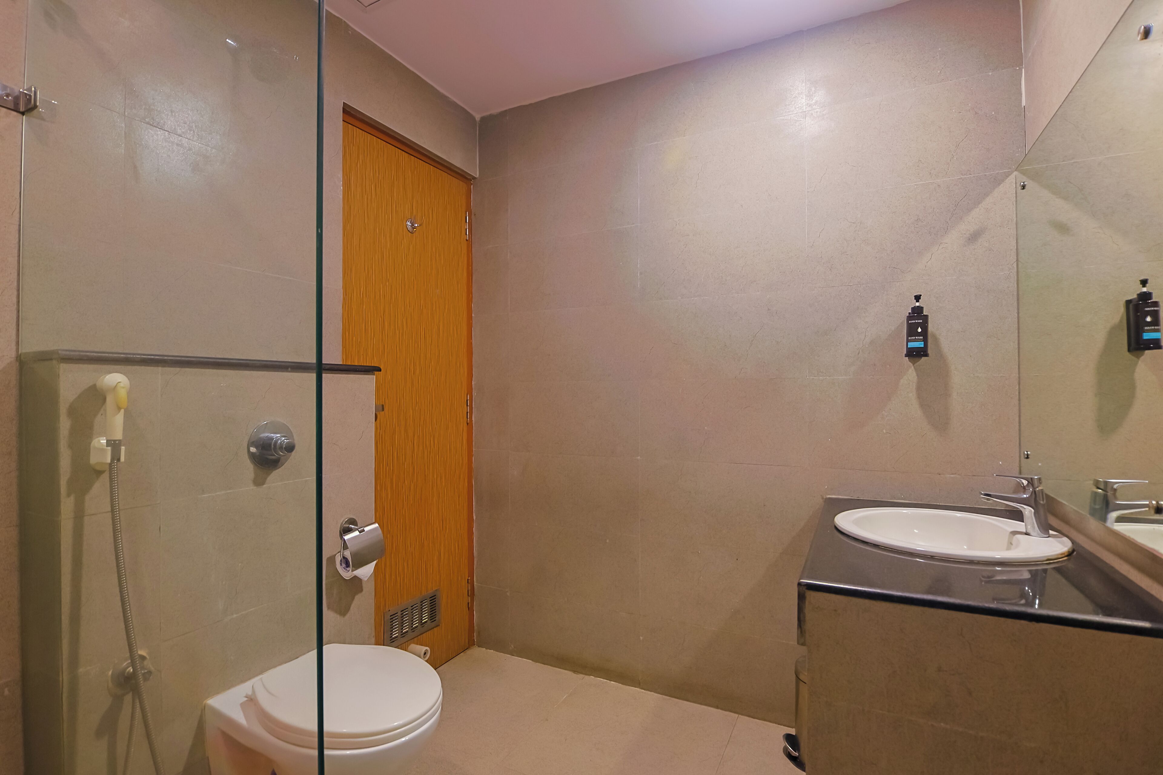A compact bathroom with a toilet, a glass shower enclosure, a sink, and a wooden door.