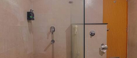 Une salle de bain avec une douche à parois de verre, des toilettes et un seau rouge.