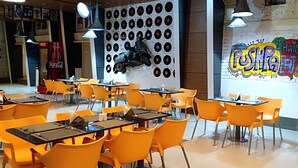 Interior de restaurante con sillas y mesas anaranjadas, una pared llena de discos de vinilo y una pared con grafitis de colores.