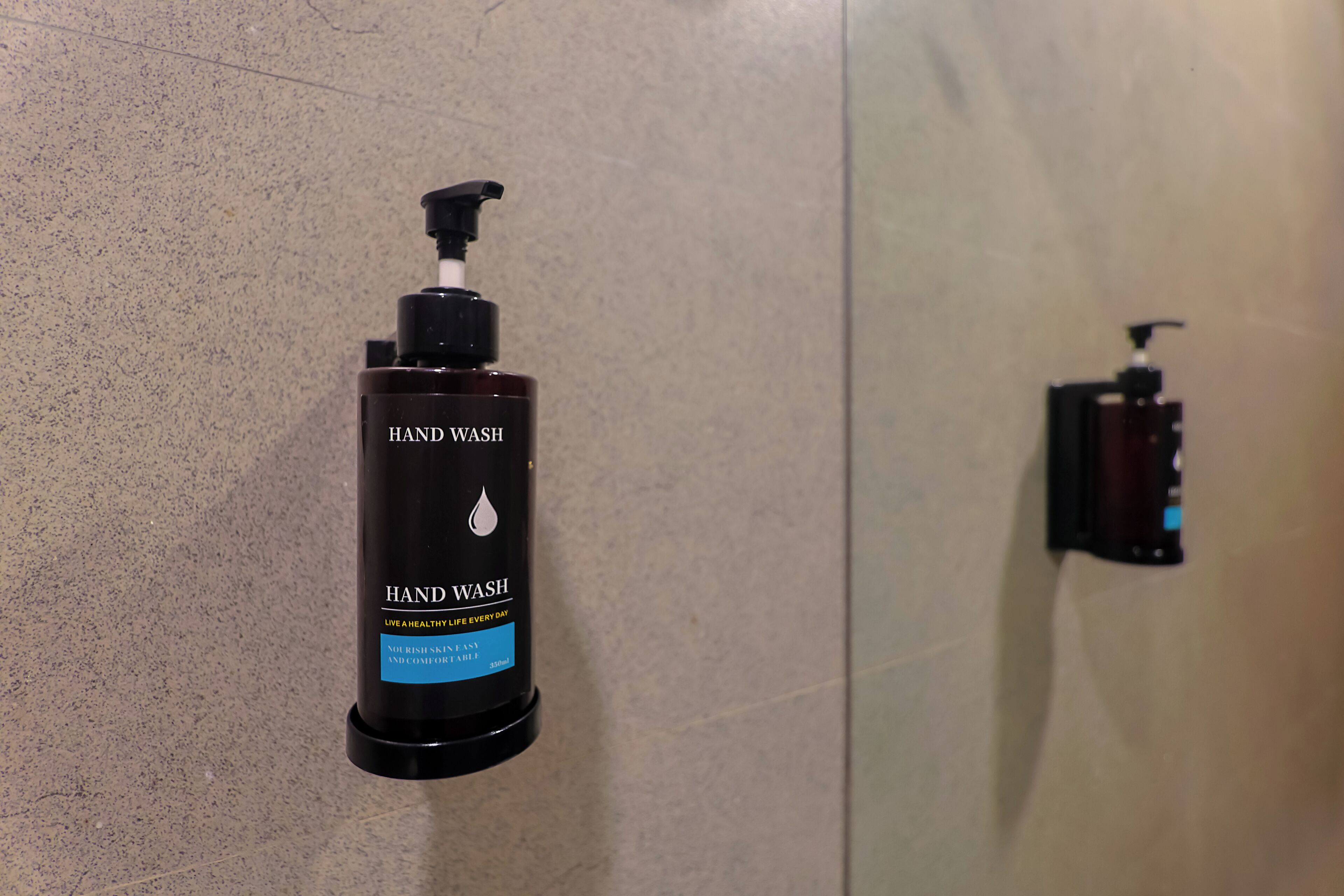 A hand wash dispenser mounted on a wall in a bathroom.