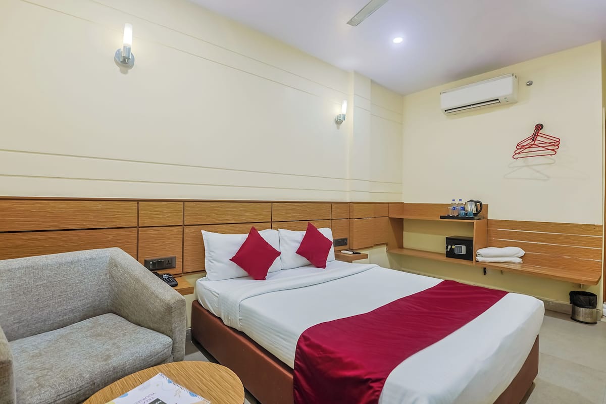 Habitación de hotel con cama, sofá, mesita de noche, aire acondicionado de pared y estante con toallas y un radio.