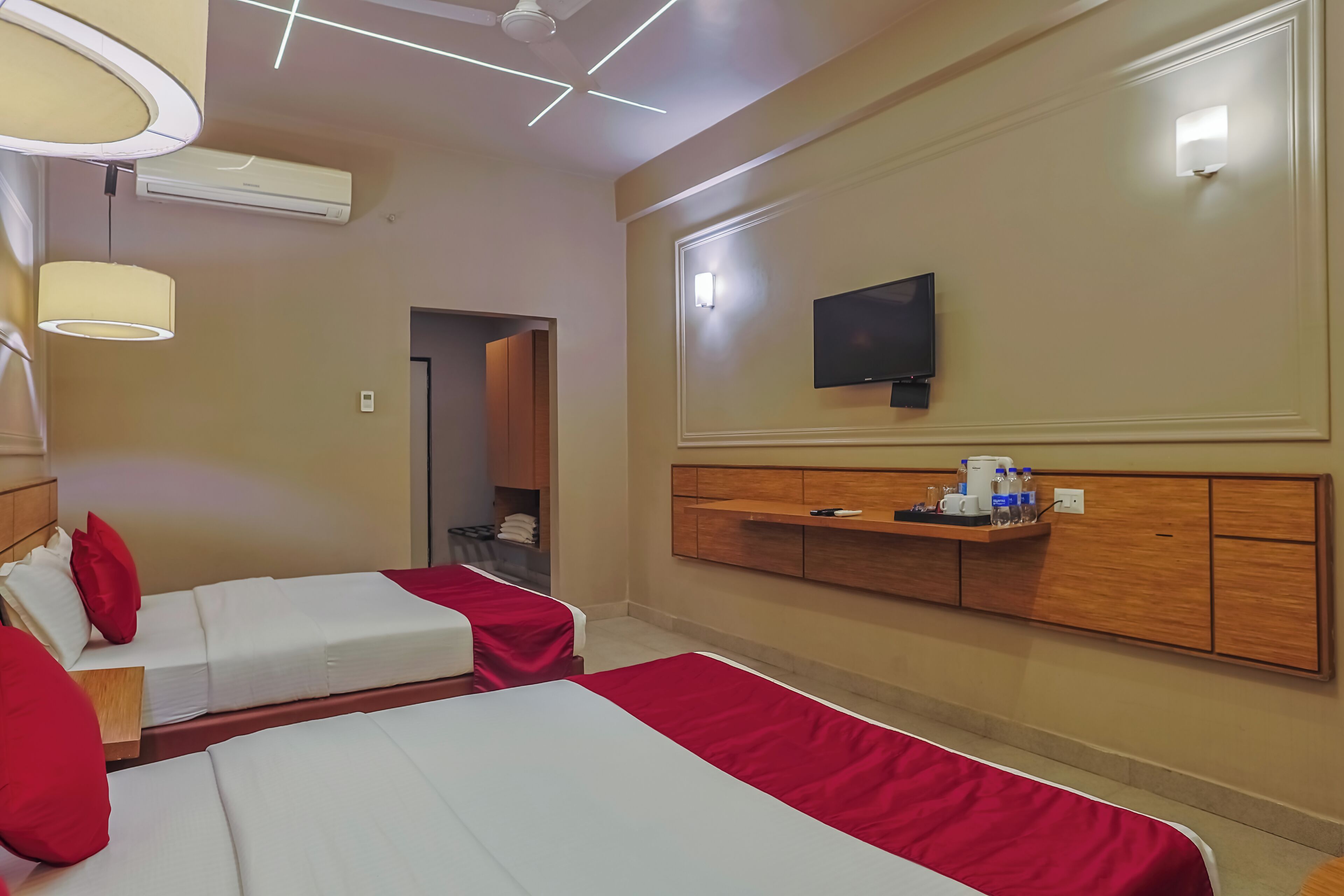 Habitación de hotel con dos camas, televisión, minibar y ventilador de techo.