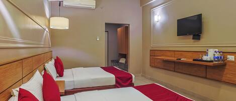 A hotel room with two beds, a TV, a shelf with toiletries, and a ceiling fan.