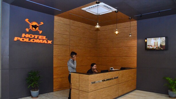 Un mostrador de recepción de hotel con detalles de madera, un logotipo en la pared y una pantalla de televisión encima.