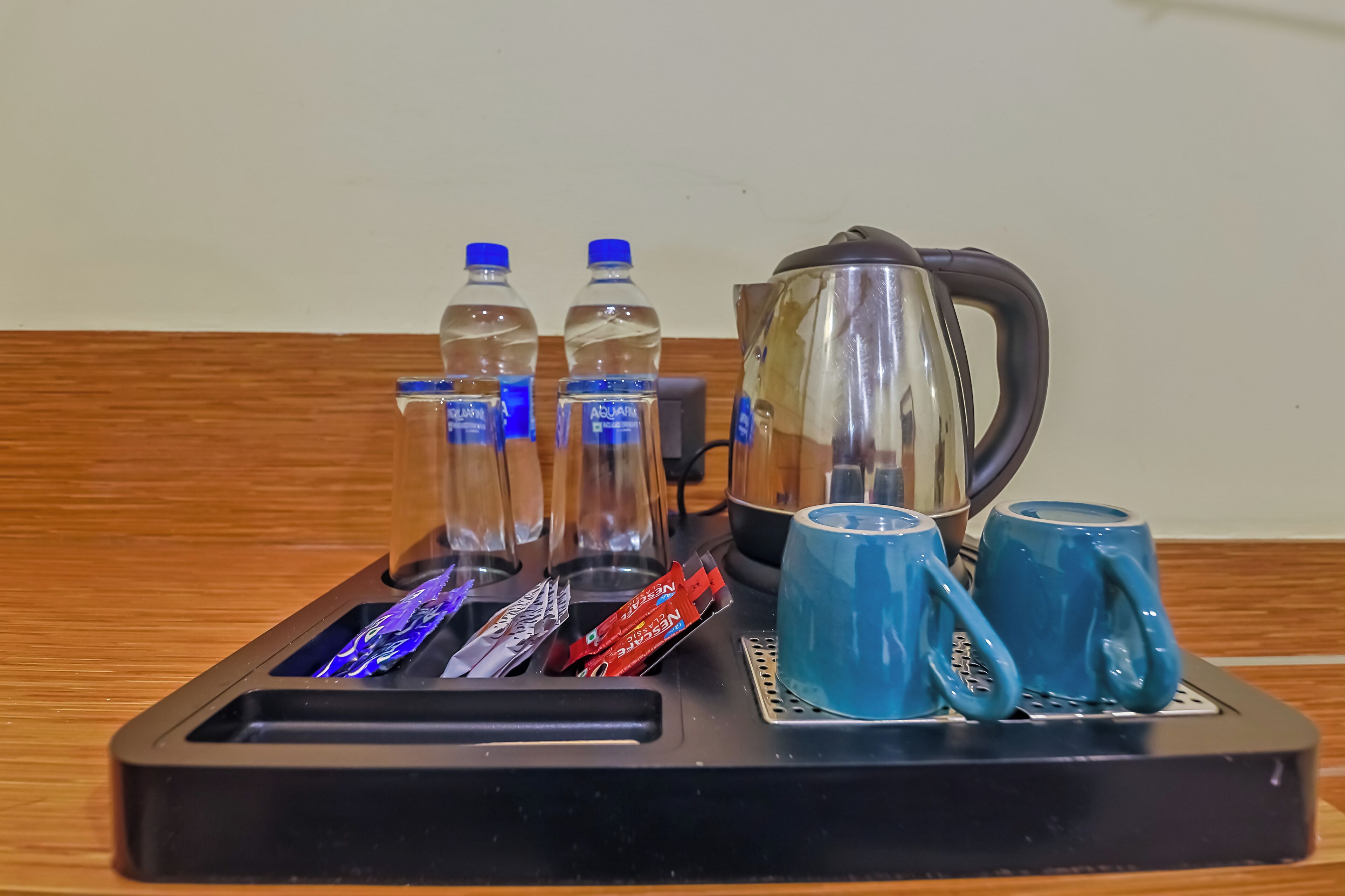 A tray with a kettle, two water bottles, two glasses, and a mug.