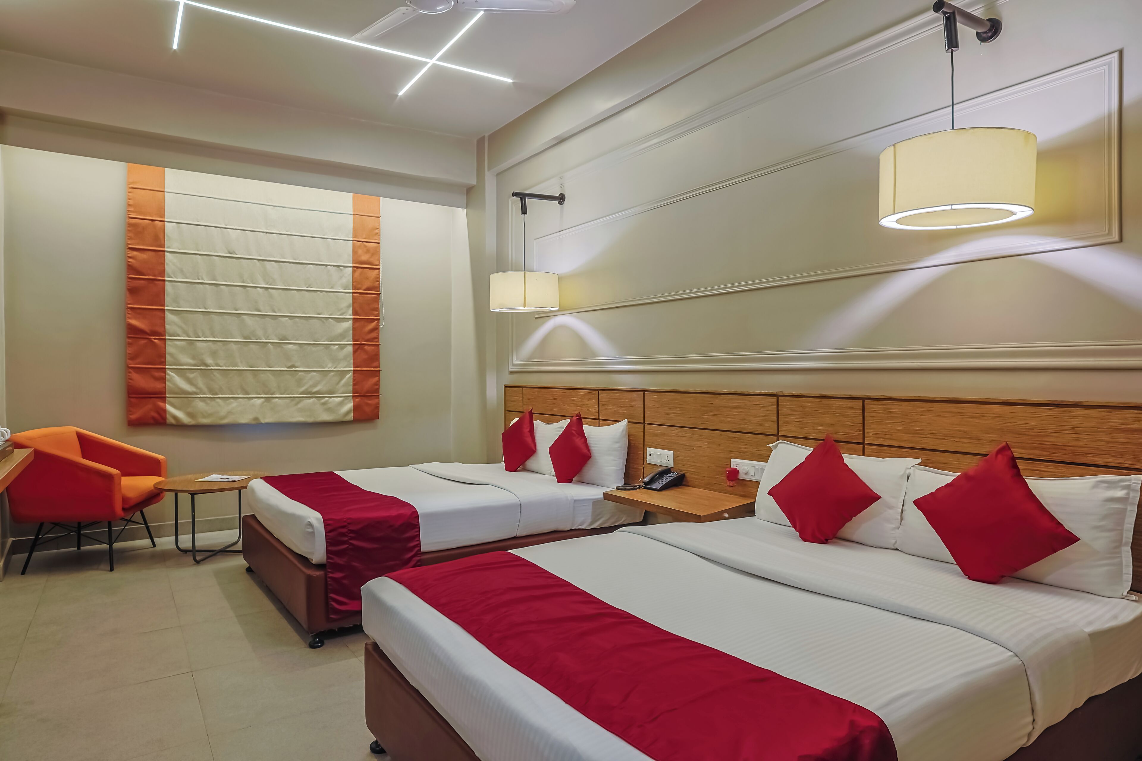 A hotel room with two beds, a red chair, a small table, and a large window with a curtain.