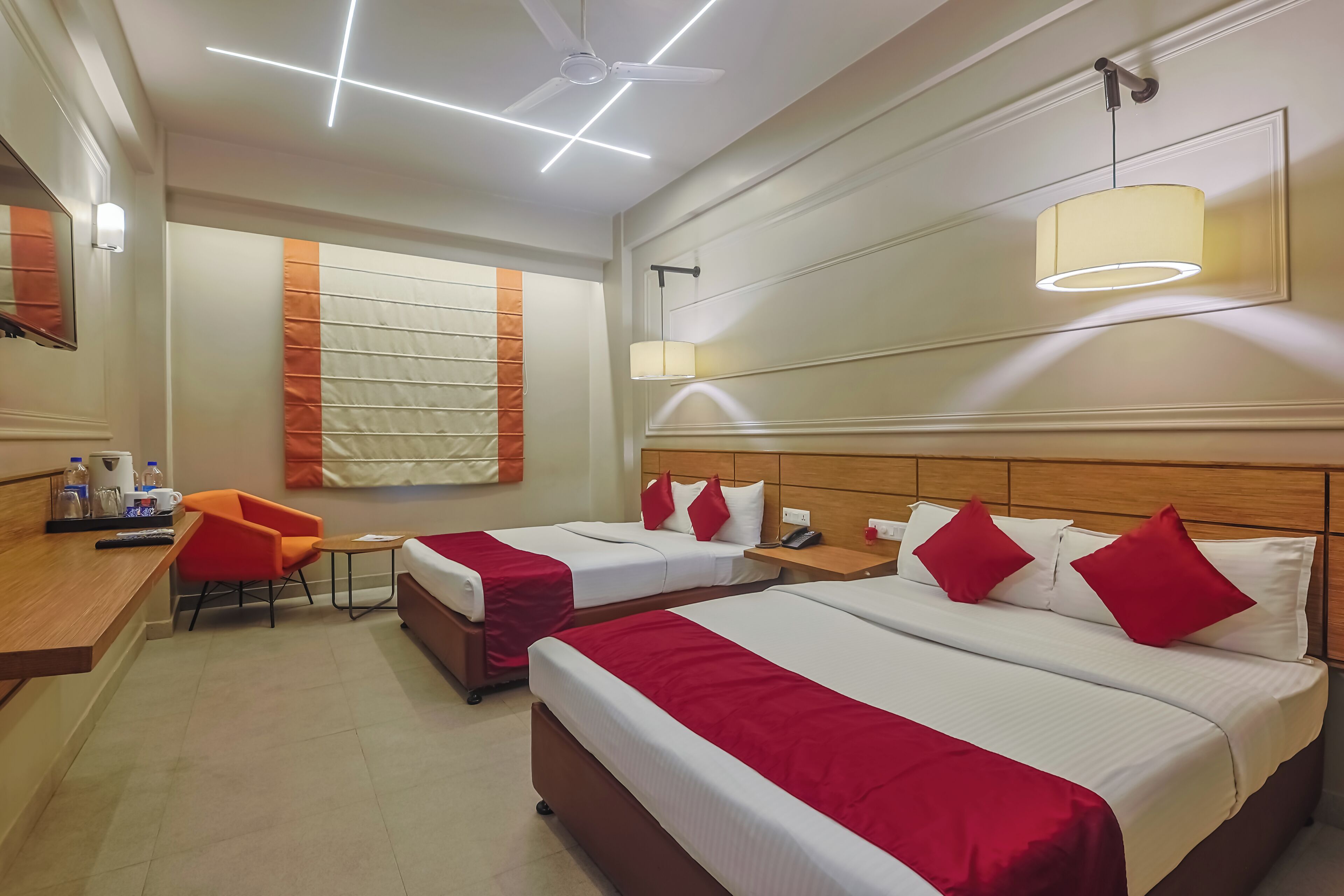 A hotel room with two beds, a desk, a chair, a ceiling fan, and a large window with blinds.