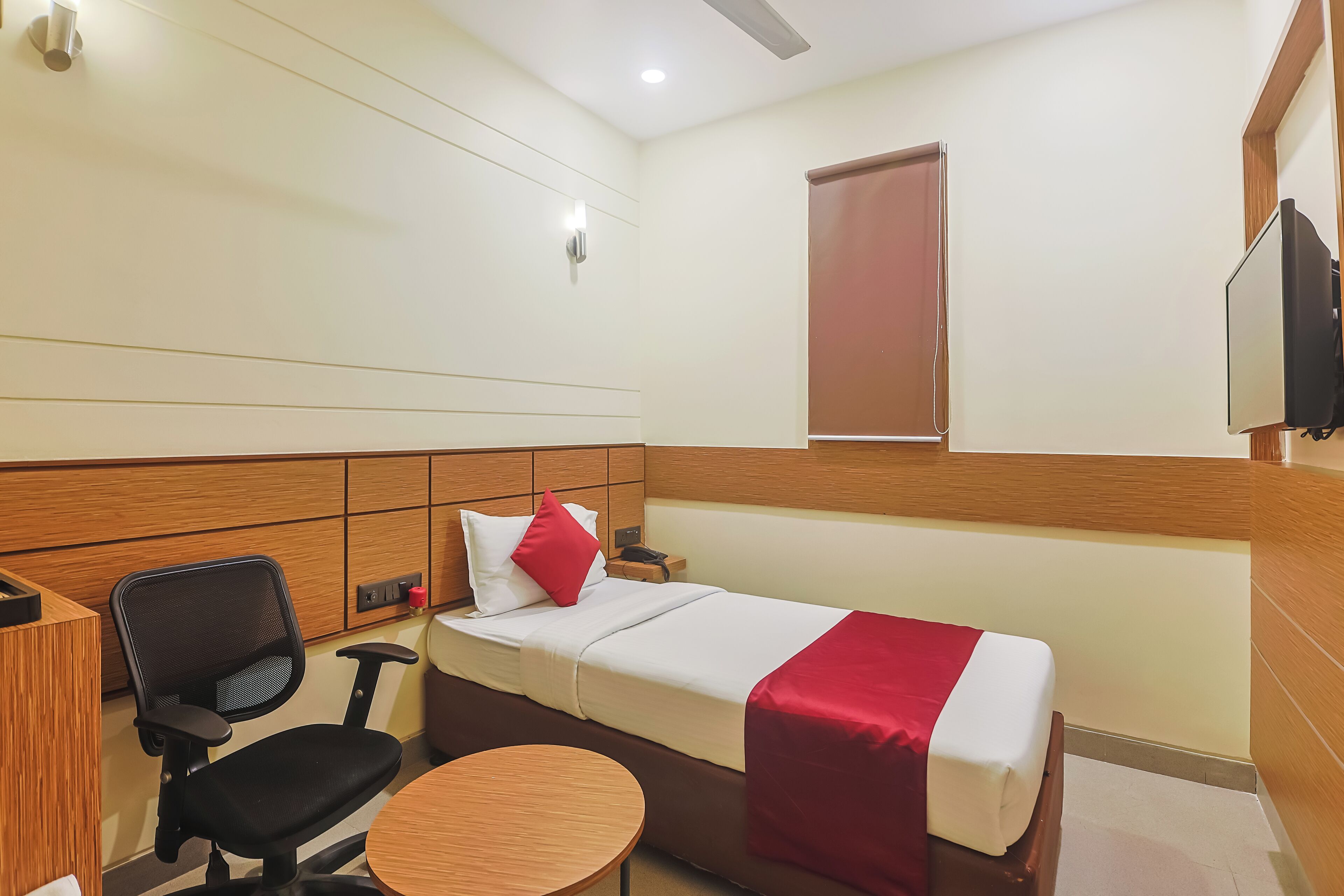 A hotel room with a bed, a desk, a chair, a small table, and a TV.