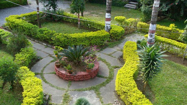 A garden with a circular stone pathway, surrounded by neatly trimmed hedges and various plants. - Green Park (Pokhara)