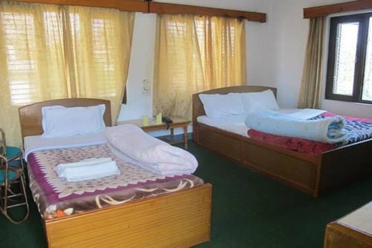 A hotel room with two single beds, a wooden headboard, a small table, and a window with curtains.