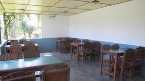 A room with wooden tables and chairs, a tiled ceiling, and a window with a view of greenery outside. - Green Park (Pokhara)