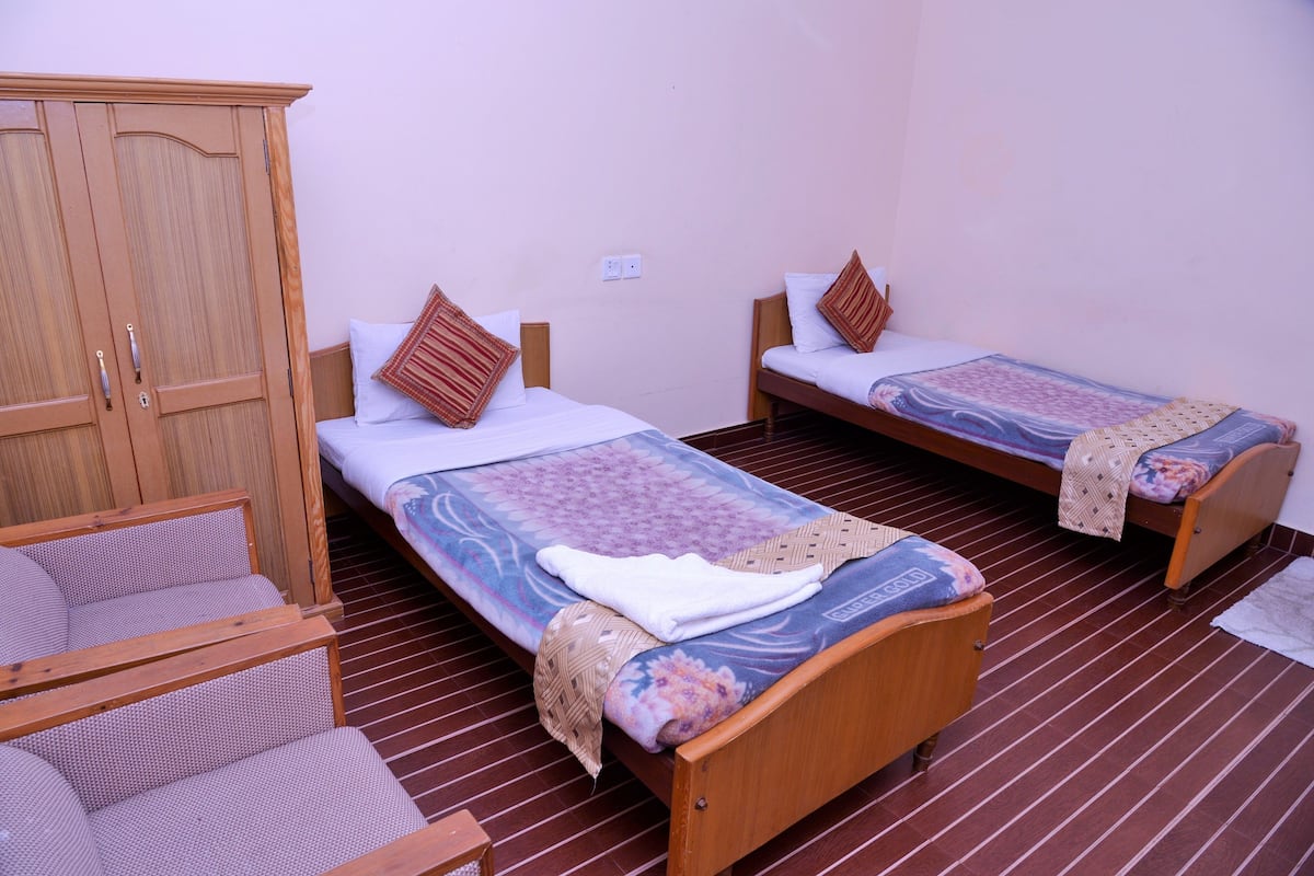 A room with two single beds, a wooden wardrobe, and a chair.