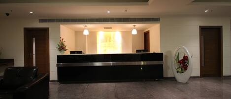 A reception area with a reception desk, two pendant lights, a large floral arrangement, and a black leather sofa.