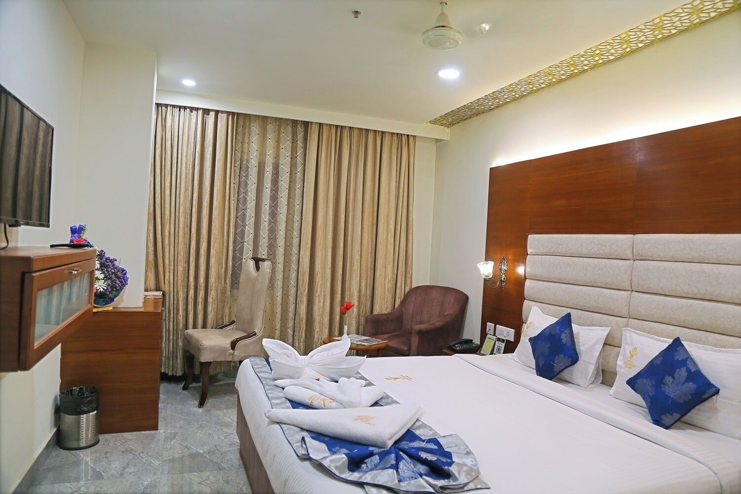 A hotel room with a bed, a desk, a chair, a TV, and curtains.