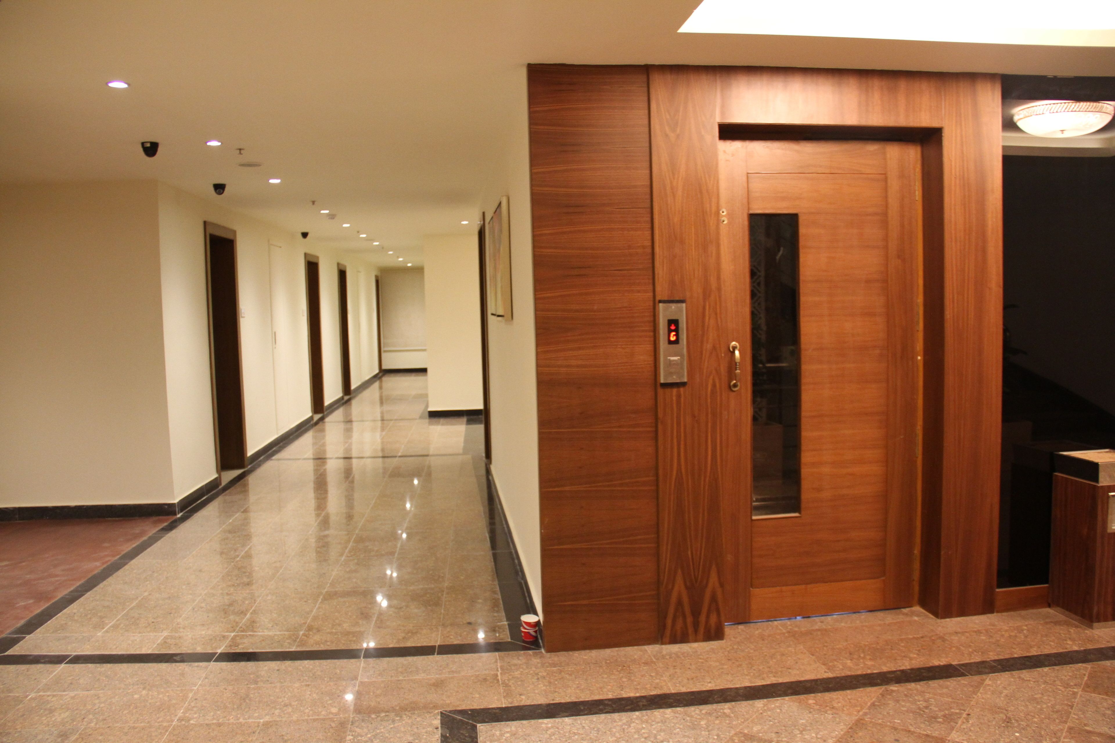 A long, polished hallway with a wooden elevator and a visible elevator control panel.