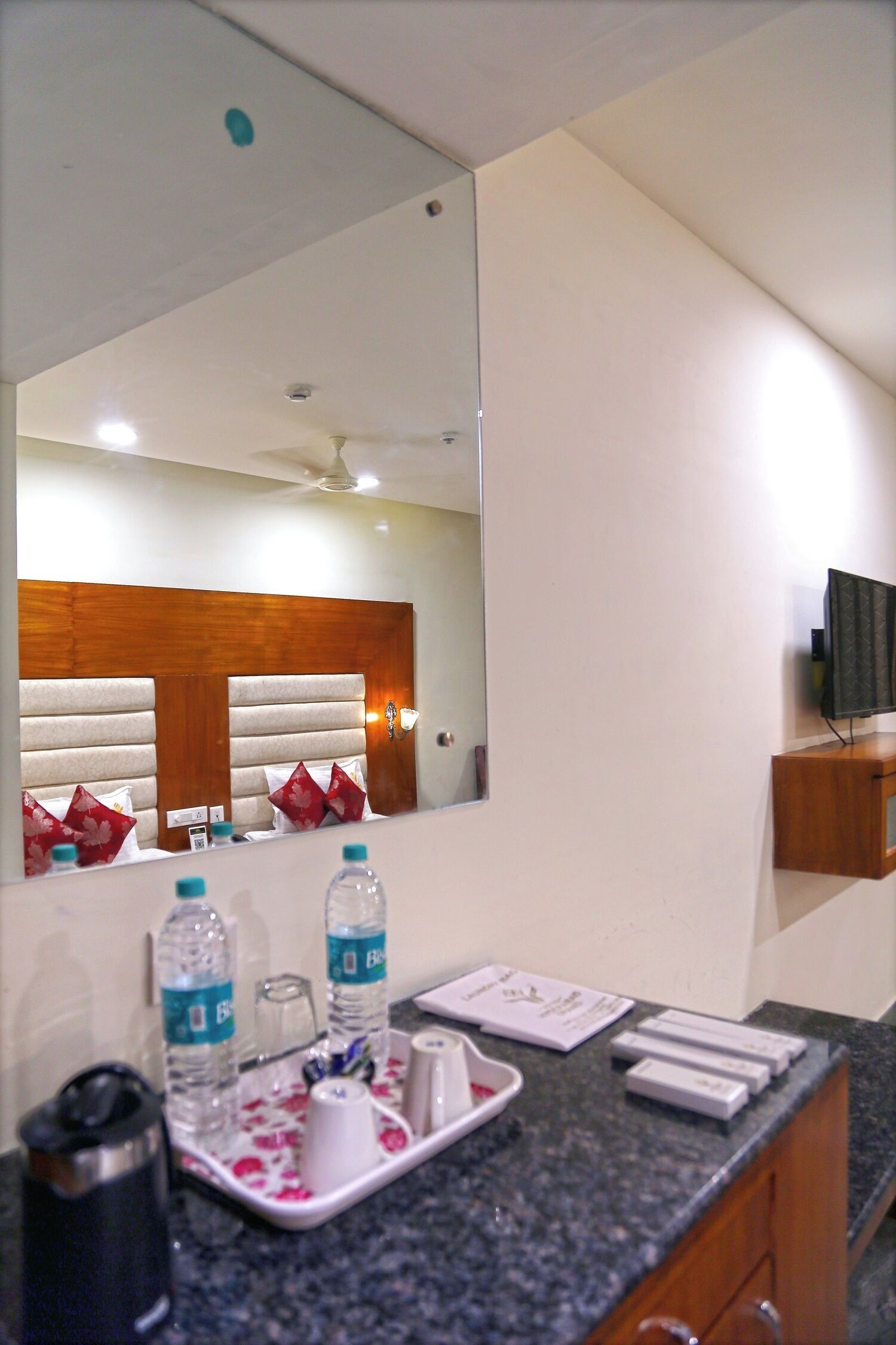 A hotel bathroom with a large mirror, a sink with toiletries, and a television mounted on the wall.
