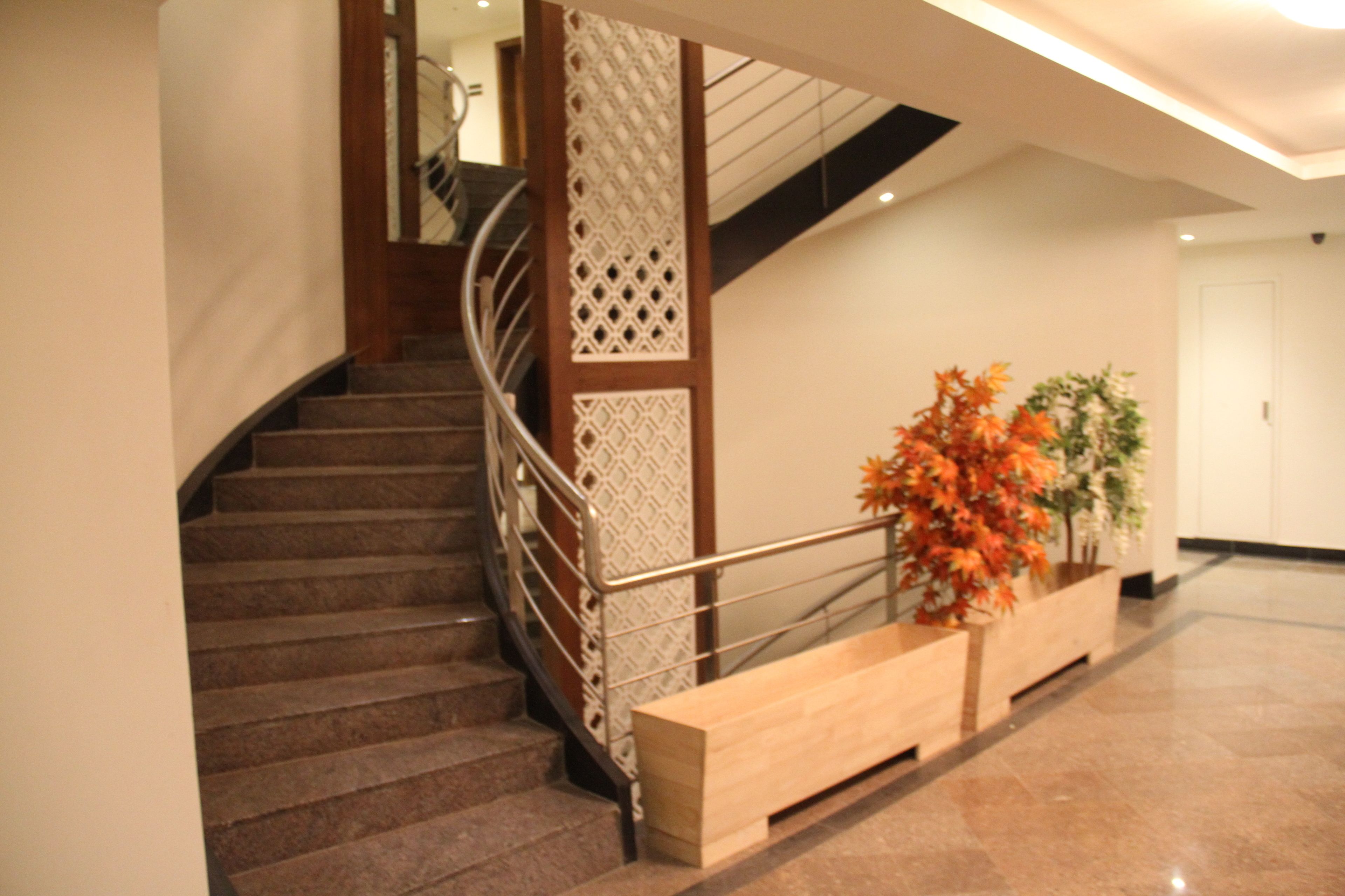Una escalera con barandilla de madera y un panel decorativo, que conduce a un rellano con un banco y una planta en maceta.
