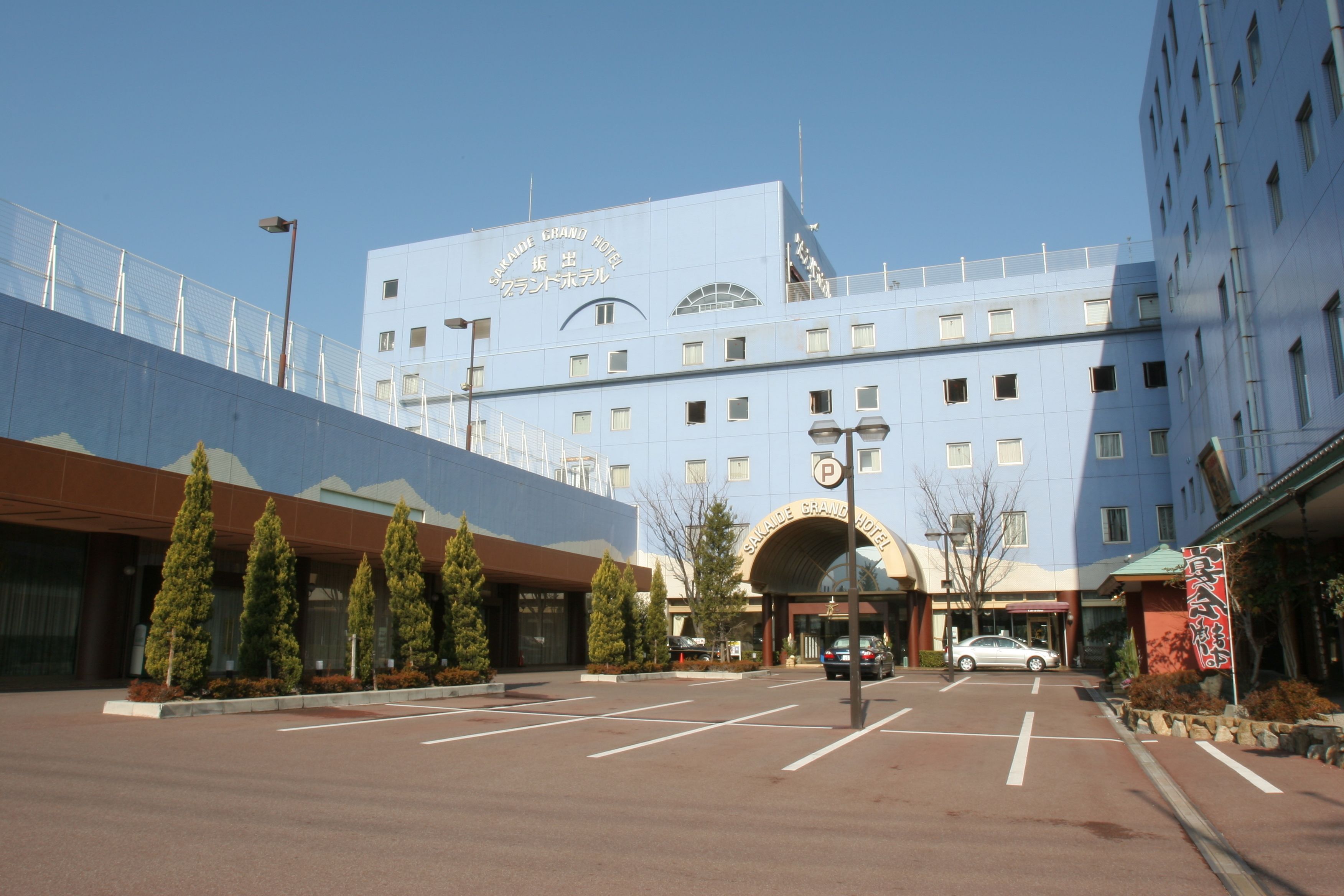 Un hôtel avec une grande façade bleue, un parking et un ciel dégagé.