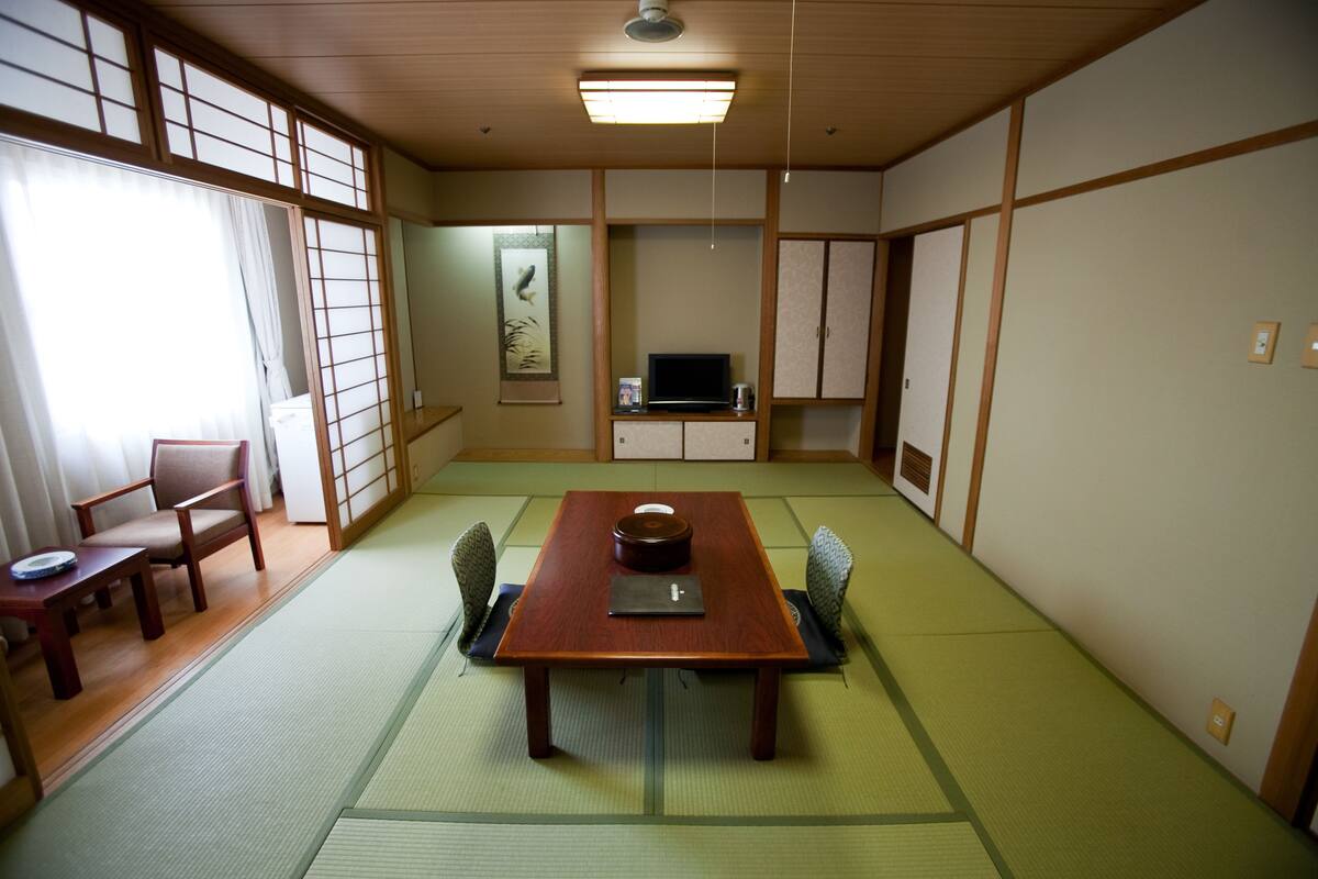 A traditional Japanese room with tatami flooring, a low table with a laptop, a television, and a cabinet.