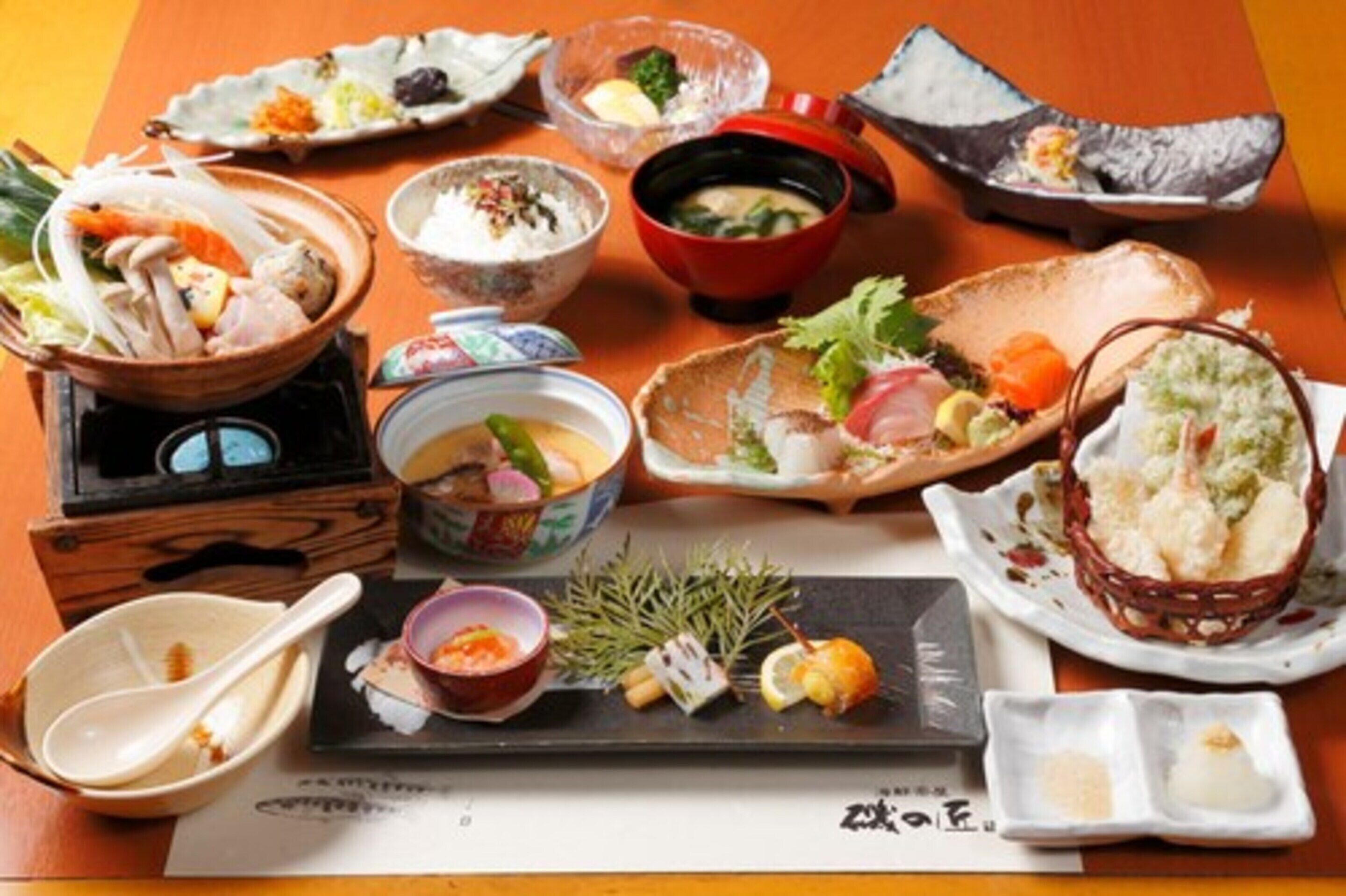 A variety of Japanese dishes on a wooden table, including sushi, sashimi, and bowls of soup.