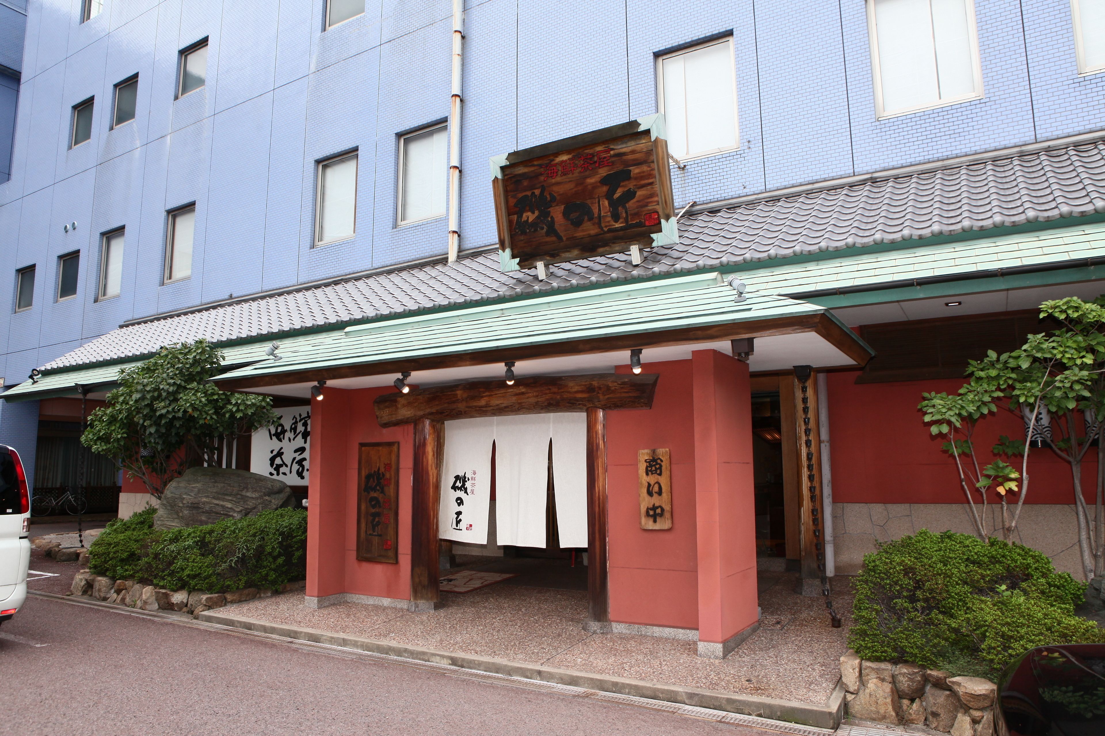 A traditional Japanese building with a wooden signboard, a tiled roof, and a stone pathway leading to the entrance.