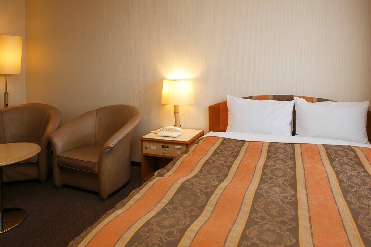 A hotel room with a bed, two chairs, a nightstand with a lamp, and a telephone.