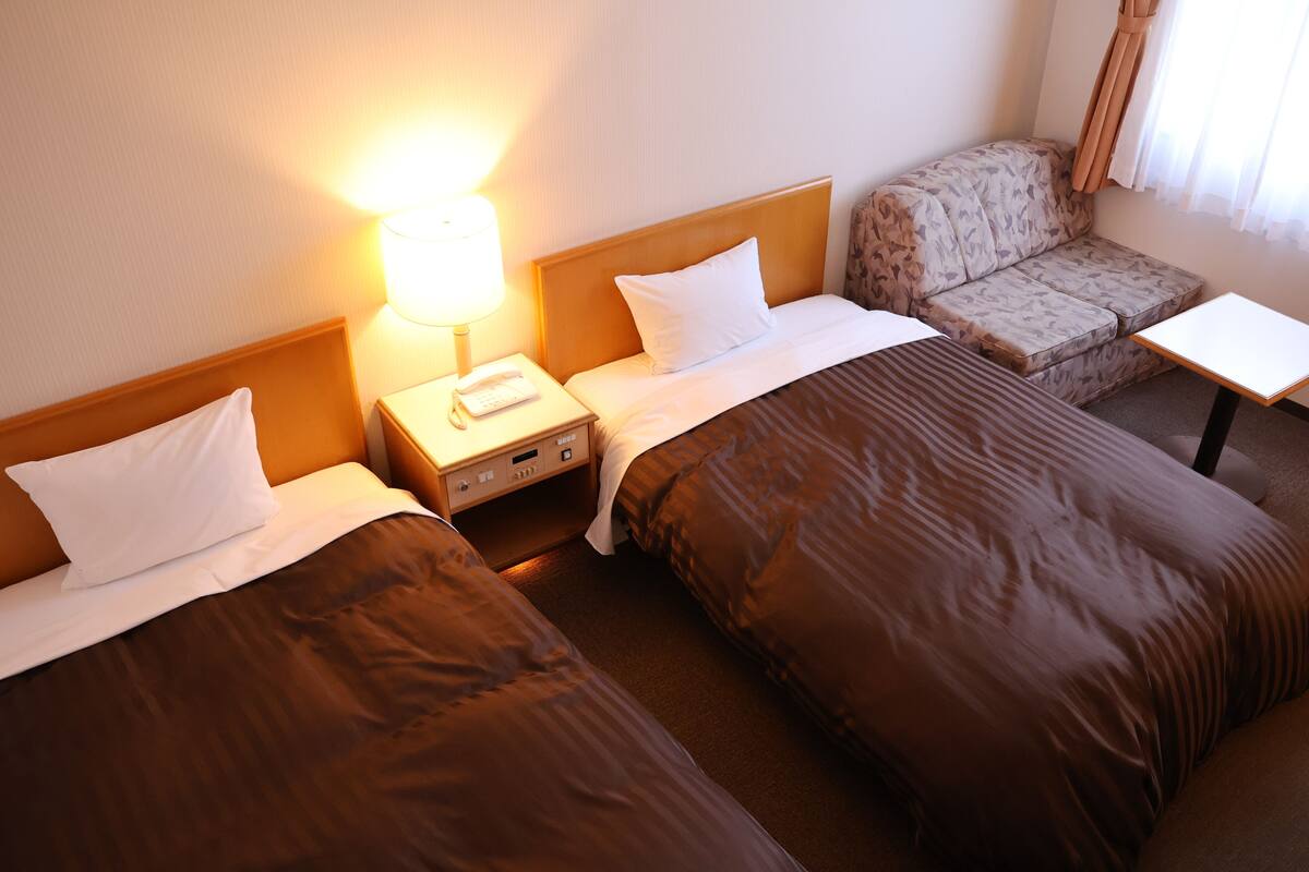 A hotel room with two beds, a sofa, a small table, and a lamp.