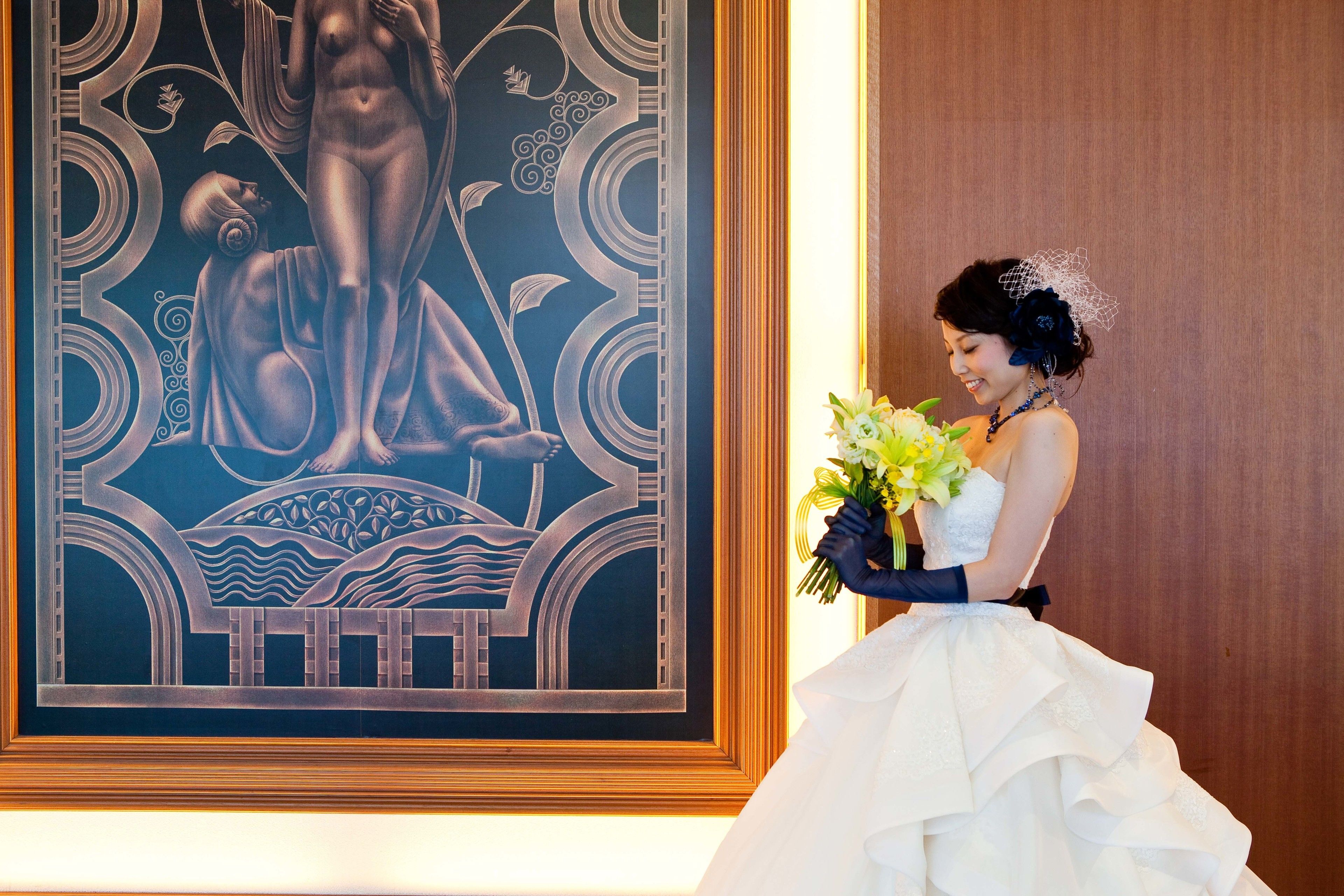 A person in a white wedding dress holding a bouquet, standing next to a large framed artwork.