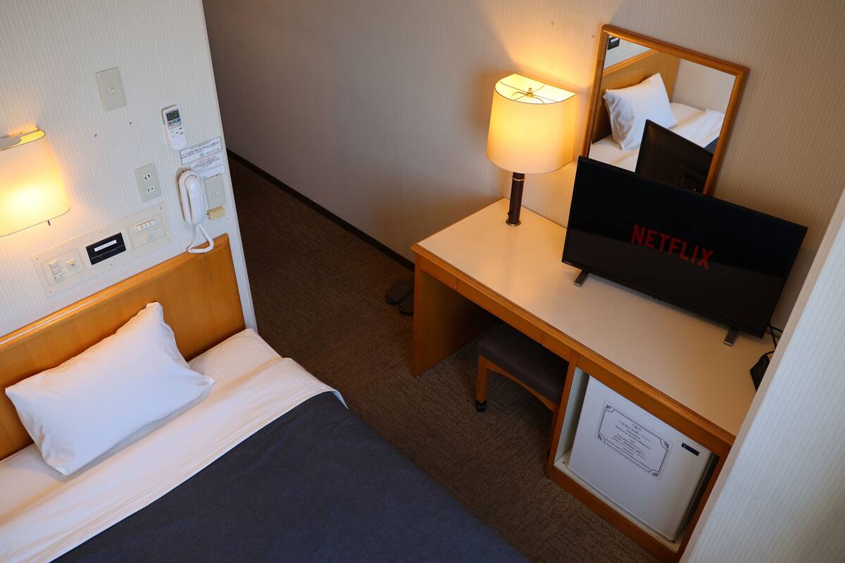 A hotel room with a bed, bedside table, lamp, TV, and a mirror.