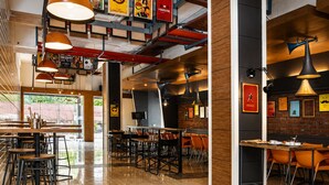 A modern restaurant interior with high ceilings, exposed beams, and a mix of metal and wooden furniture. - Max Hotels Jabalpur (Jabalpur)