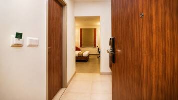 A hotel room with a bed, a desk, and a chair. There is a door on the left and a wall-mounted TV on the right.