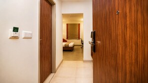 A hotel room with a bed, a desk, and a chair. There is a door on the left and a wall-mounted TV on the right. - Max Hotels Jabalpur (Jabalpur)