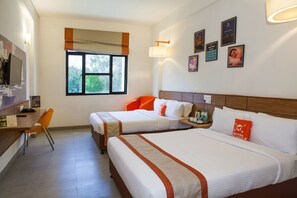 Habitación de hotel con dos camas, un escritorio con silla, una ventana y obras de arte en la pared.