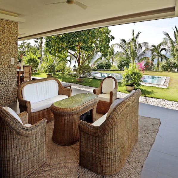 A wicker outdoor seating area with a table, overlooking a pool and lush greenery. - Les Maisons D'itac (Ronda)
