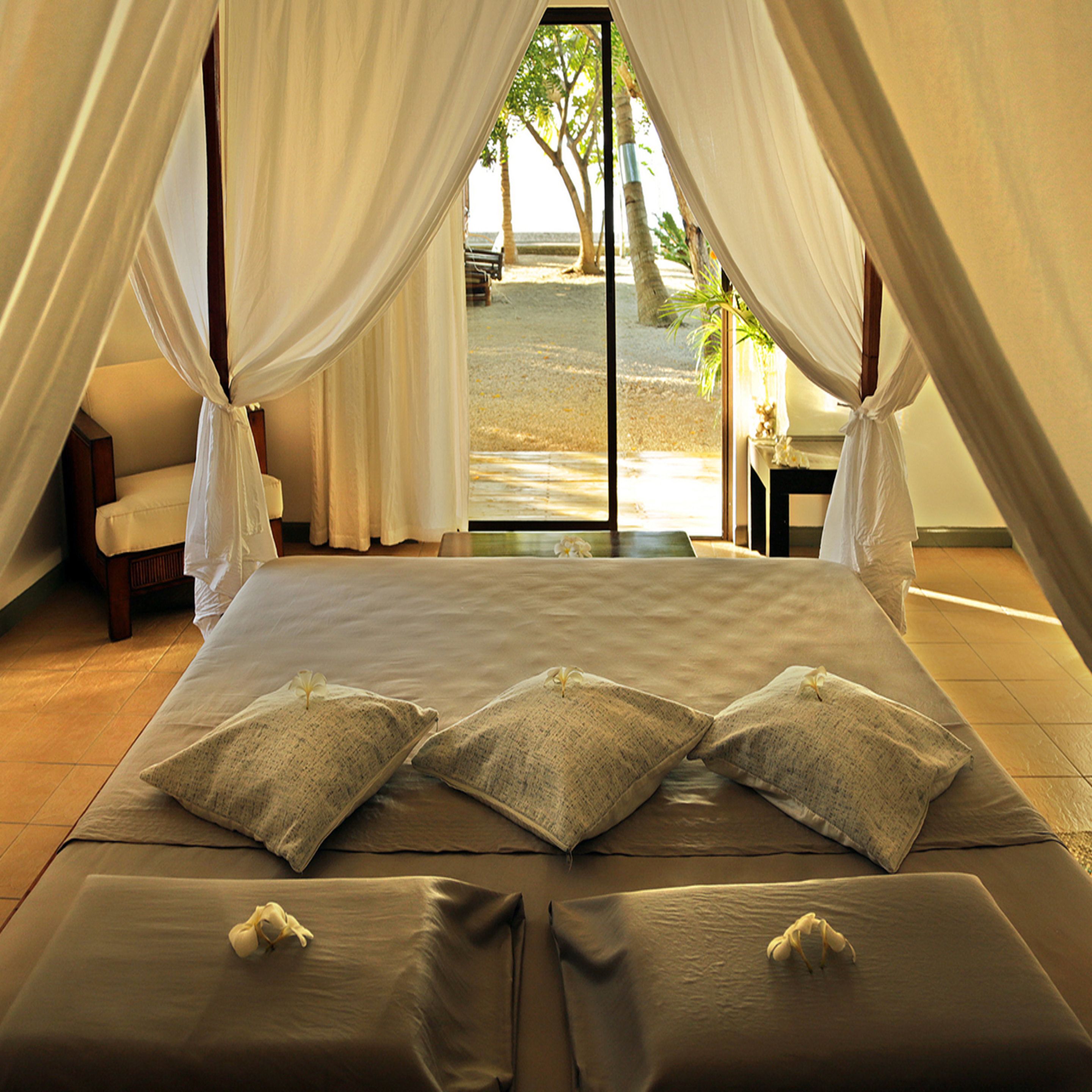 A bed with a canopy, pillows, and a view of the beach.